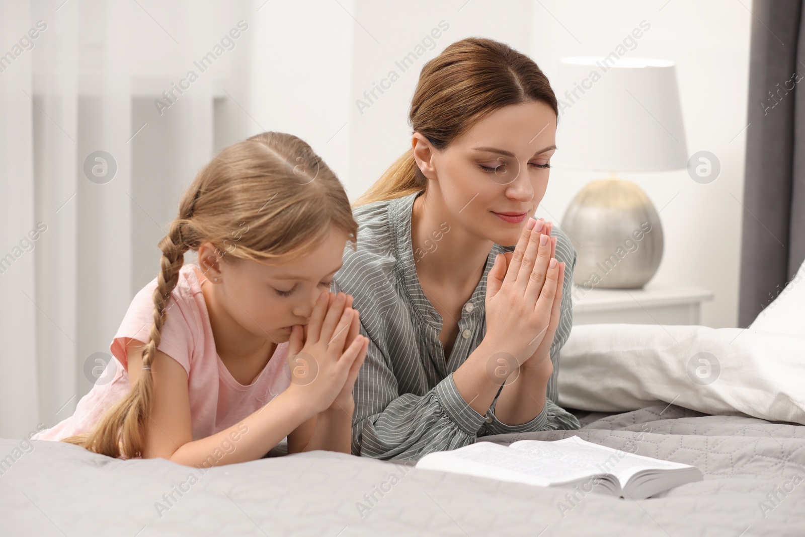 Photo of Girl and her godparent praying over Bible together at home