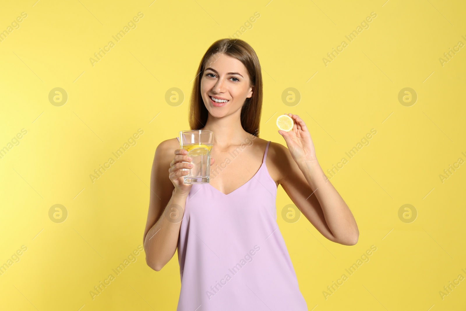 Photo of Young woman with glass of lemon water on yellow background