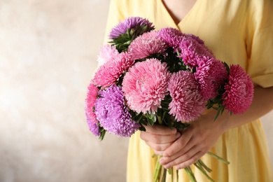 Photo of Woman holding bouquet of beautiful aster flowers on beige background, closeup. Space for text