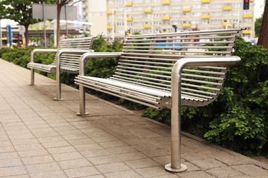 Stylish metal benches near coniferous plants on city street