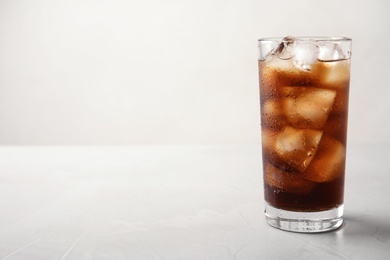 Photo of Glass of refreshing cola with ice on light table. Space for text