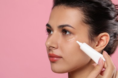Photo of Woman applying cream under eyes on pink background, closeup. Skin care, space for text