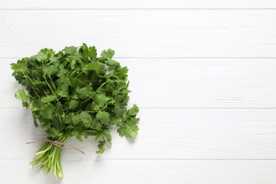 Photo of Bunch of fresh aromatic cilantro on white wooden table, top view. Space for text