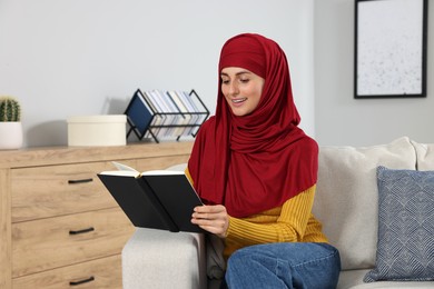 Muslim woman reading book on couch in room