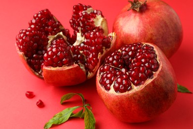 Photo of Fresh pomegranates and green leaves on red background