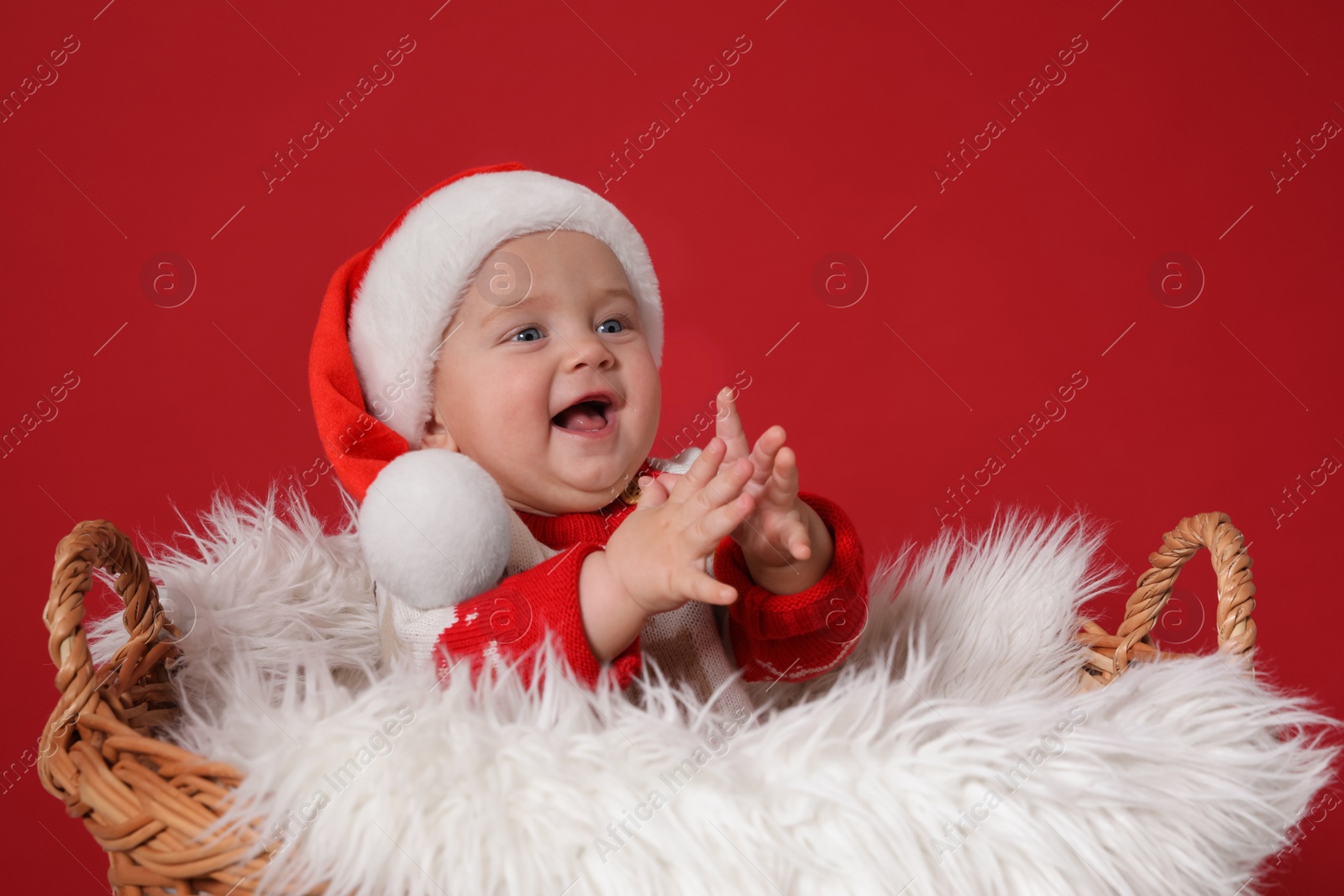 Photo of Cute baby in wicker basket on red background. Christmas celebration