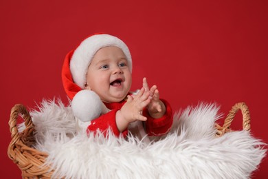 Photo of Cute baby in wicker basket on red background. Christmas celebration