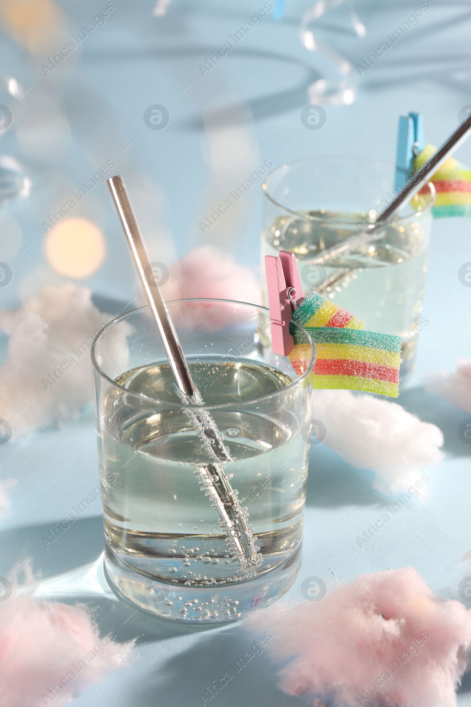 Photo of Tasty cocktails in glasses decorated with gummy candies and cotton candy on light blue background