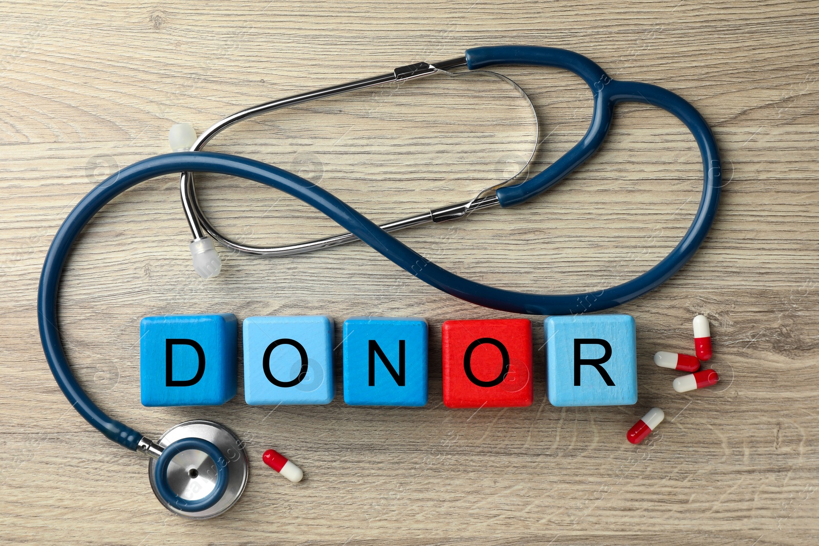 Photo of Word Donor made of cubes, stethoscope and pills on wooden table, flat lay