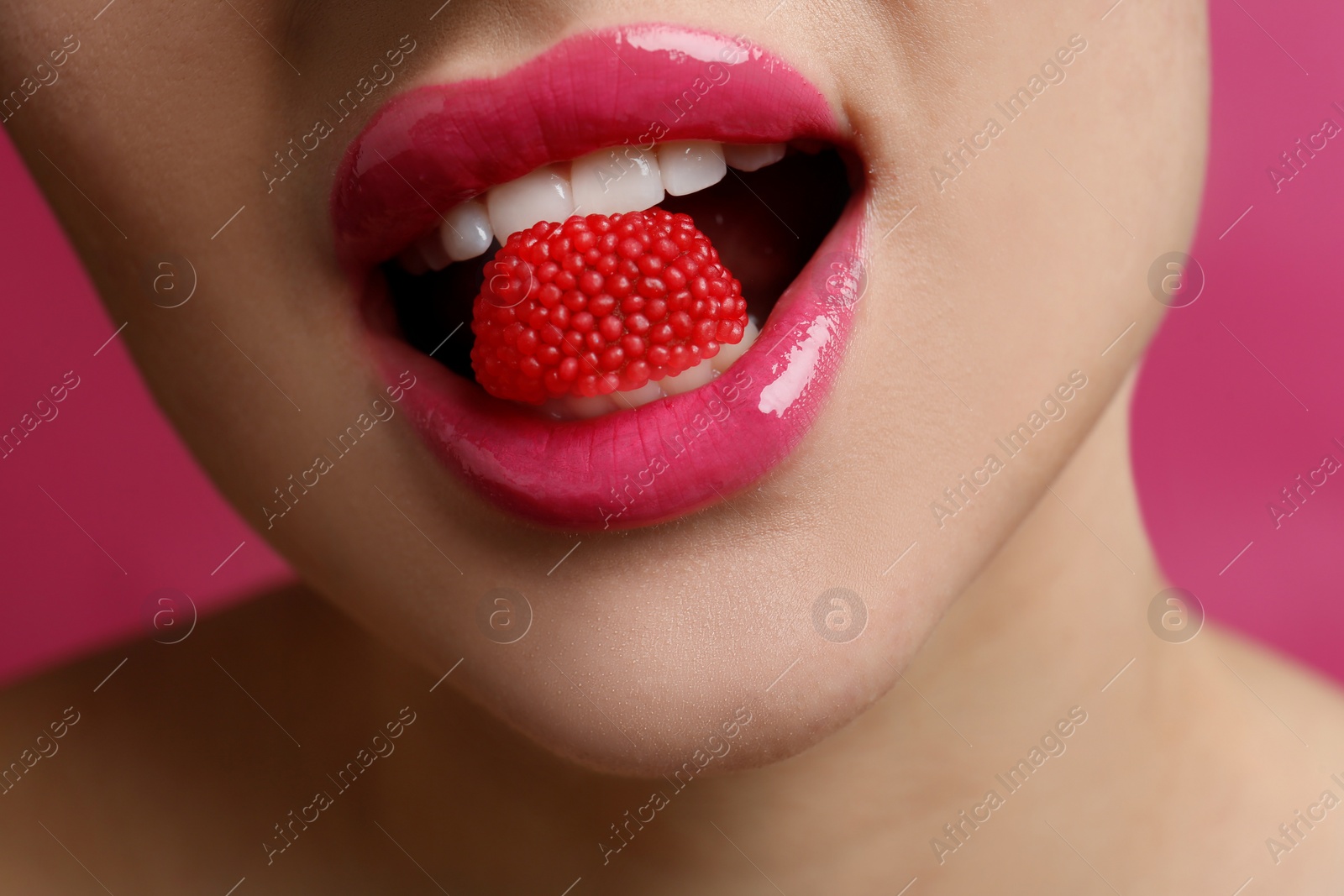 Photo of Closeup view of woman with beautiful lips eating candy on pink background