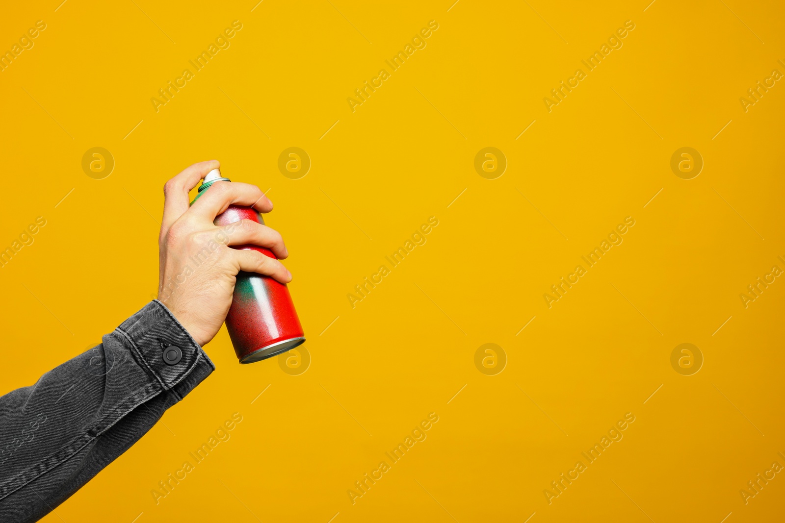 Photo of Man holding can of spray paint on yellow background, closeup. Space for text