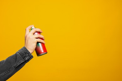 Photo of Man holding can of spray paint on yellow background, closeup. Space for text