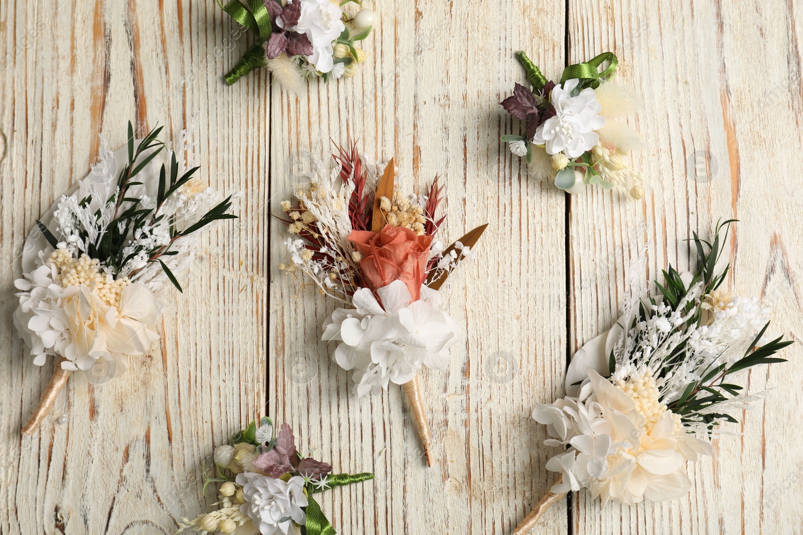 Photo of Stylish boutonnieres on light wooden table, flat lay