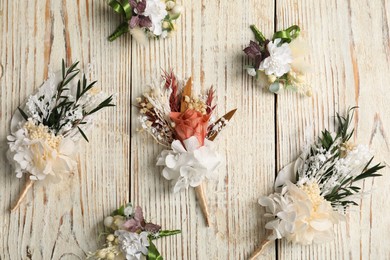 Stylish boutonnieres on light wooden table, flat lay