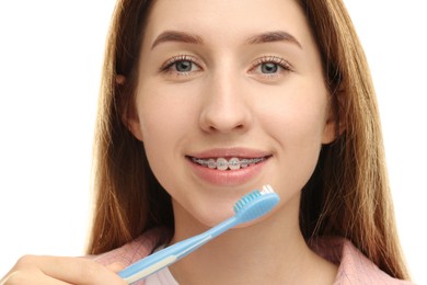 Smiling woman with dental braces cleaning teeth on white background, closeup