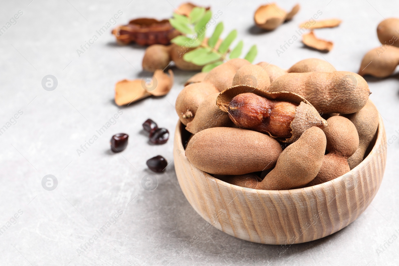 Photo of Delicious ripe tamarinds in wooden bowl on light table. Space for text