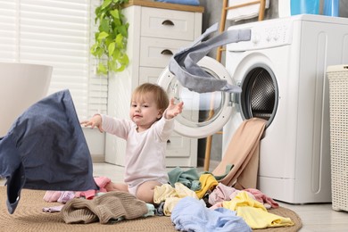 Photo of Little girl scattering baby clothes in bathroom