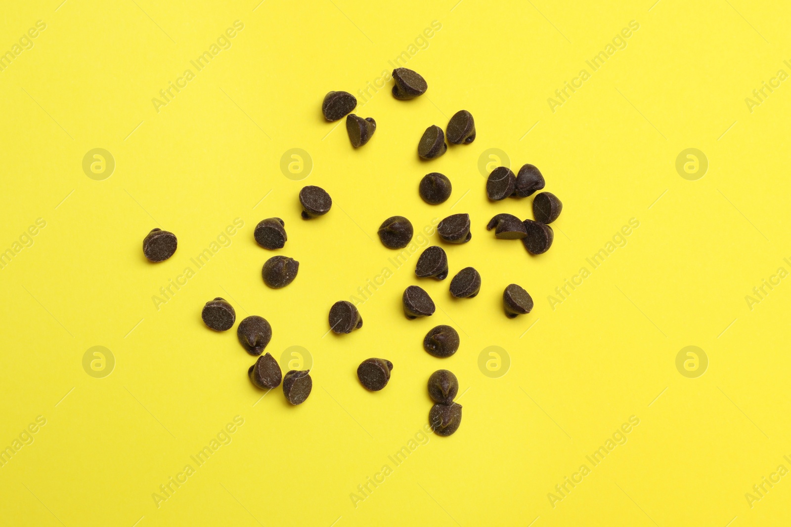 Photo of Delicious chocolate chips on yellow background, top view