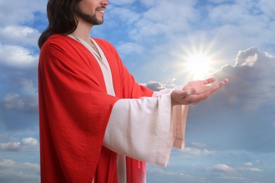 Image of Jesus Christ reaching out his hands and praying against blue sky 