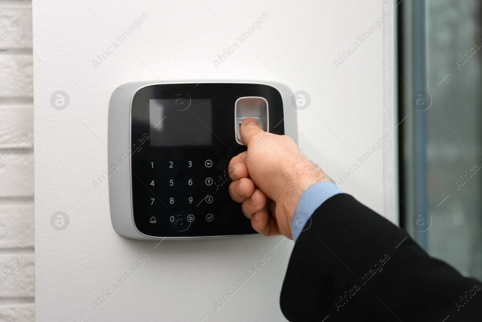 Photo of Man scanning fingerprint on alarm system indoors, closeup