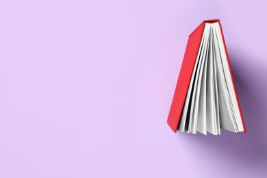 Photo of Book with red cover on violet background, top view. Space for text