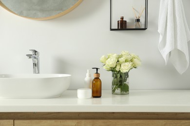 Beautiful roses and bath accessories near sink in bathroom