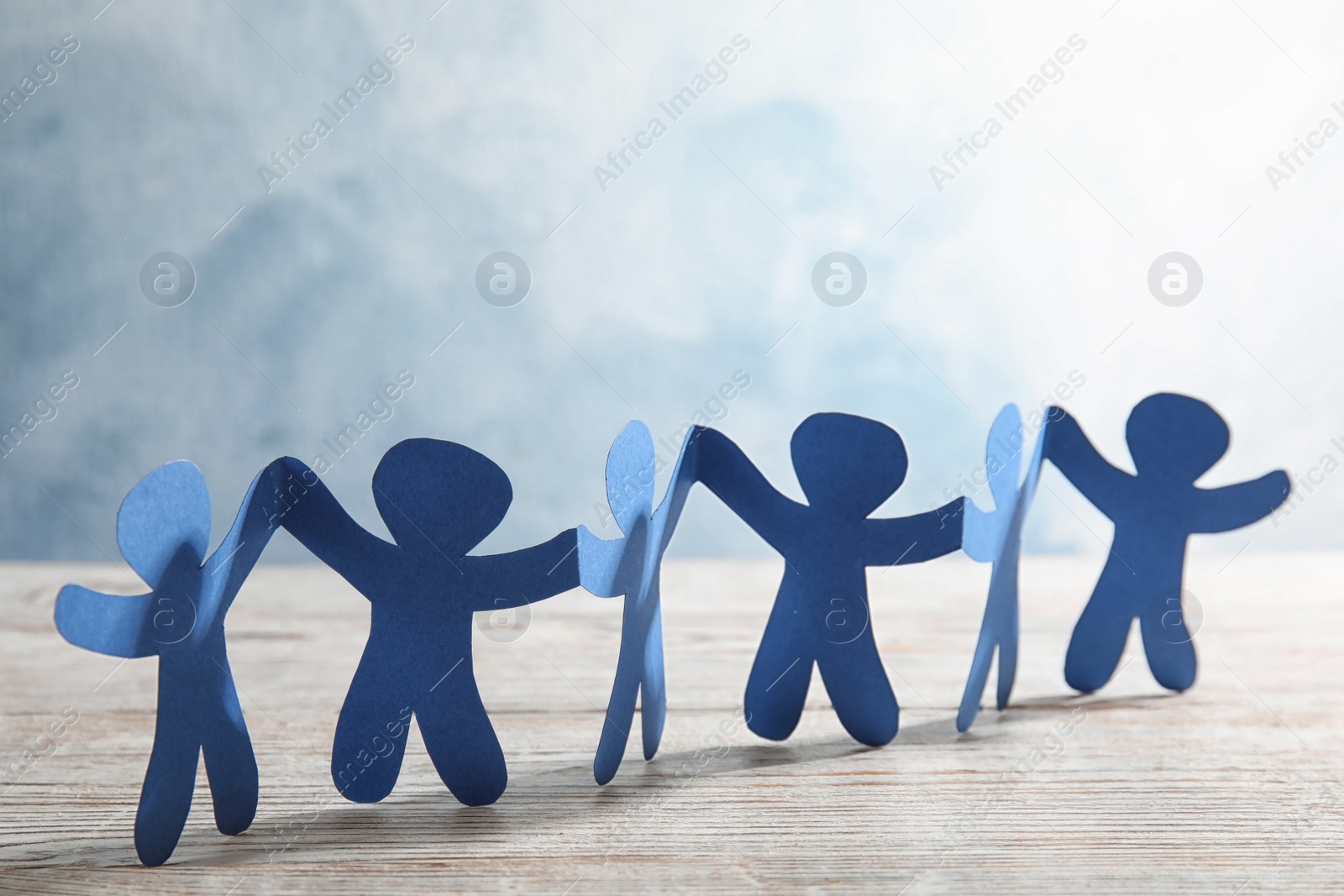 Photo of Paper people holding hands on wooden table. Unity and help concept