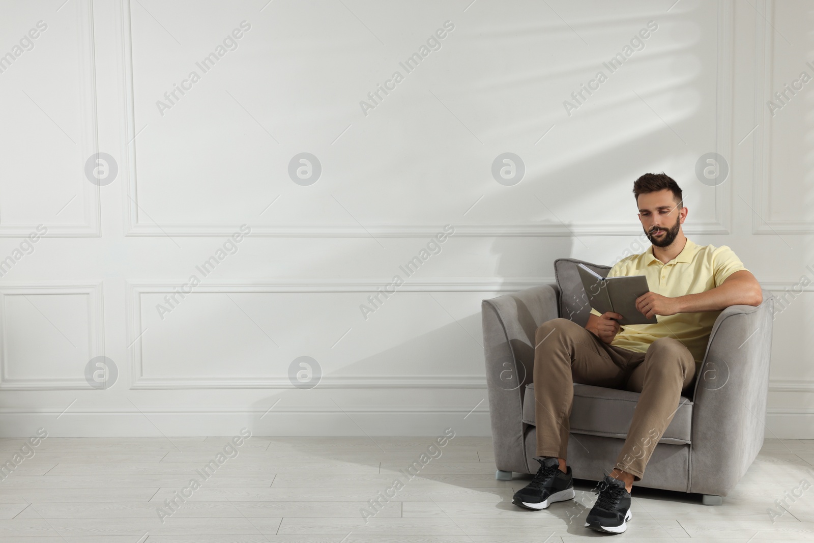 Photo of Man reading book in armchair near white wall, space for text
