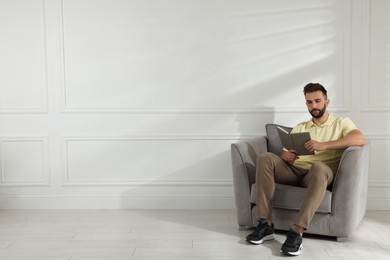Man reading book in armchair near white wall, space for text