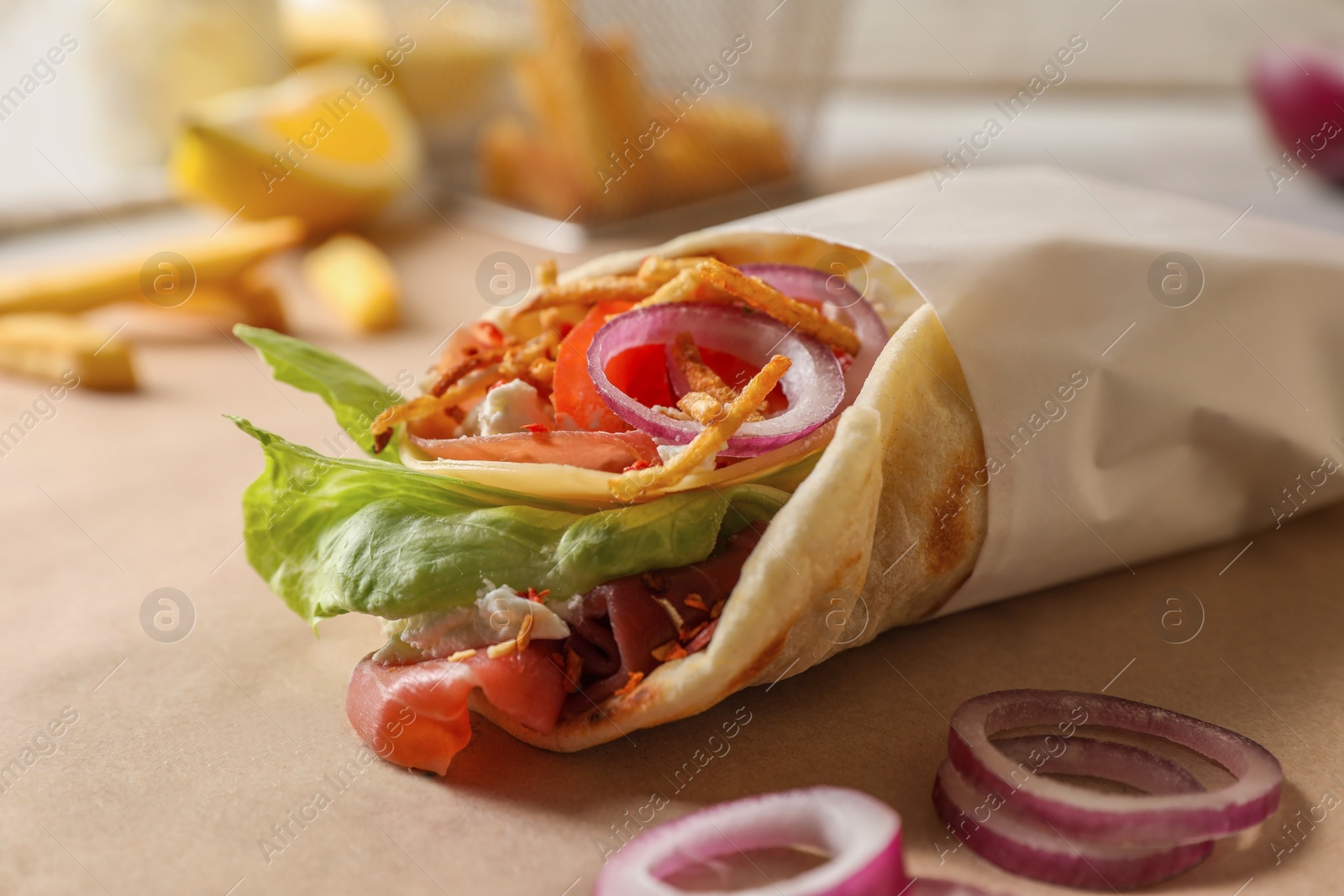 Photo of Delicious pita wrap with prosciutto and vegetables on parchment, closeup