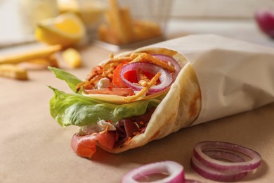 Delicious pita wrap with prosciutto and vegetables on parchment, closeup