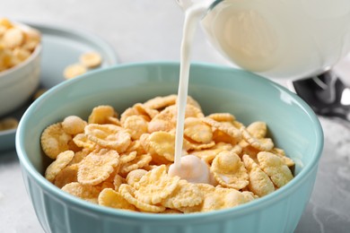 Photo of Pouring milk into bowl with cornflakes on table, closeup