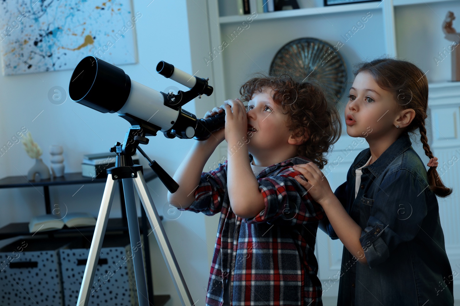 Photo of Cute little children using telescope to look at stars in room