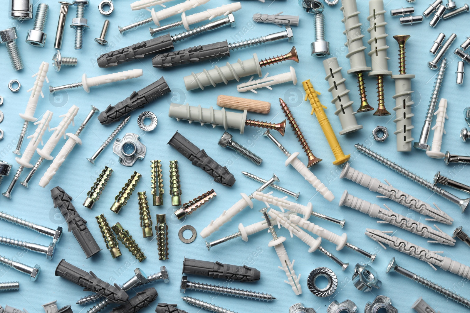 Photo of Many different fasteners and dowels on light blue background, flat lay