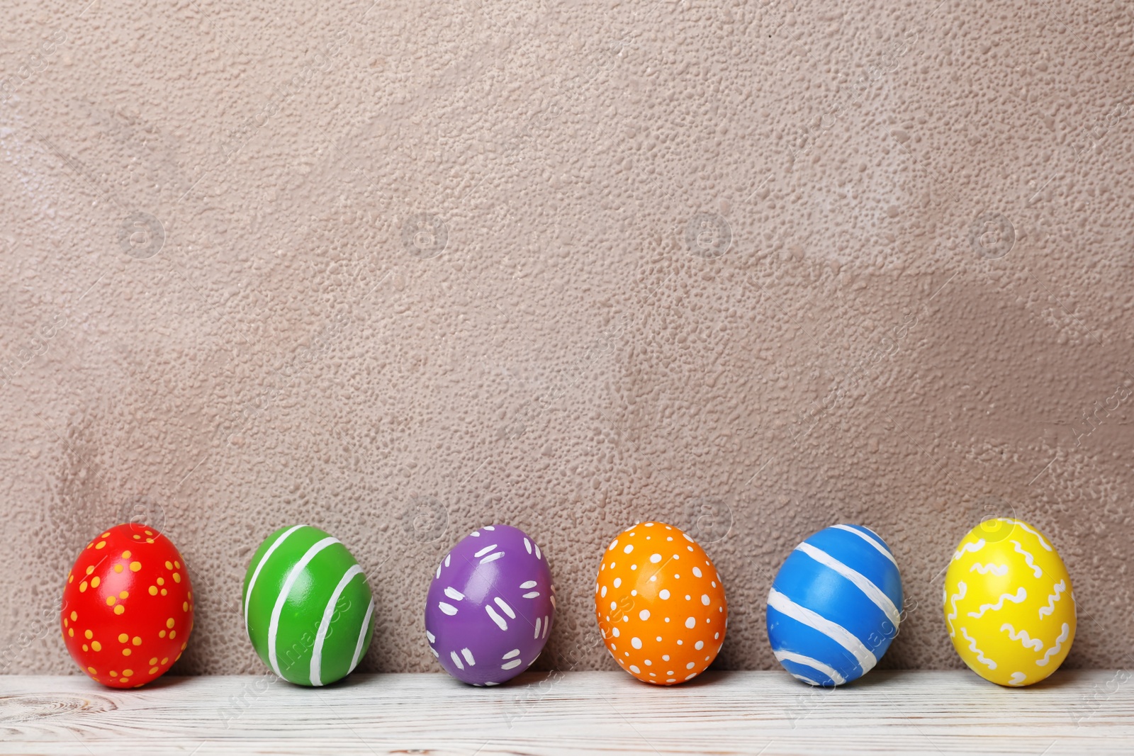 Photo of Decorated Easter eggs on table near color wall. Space for text