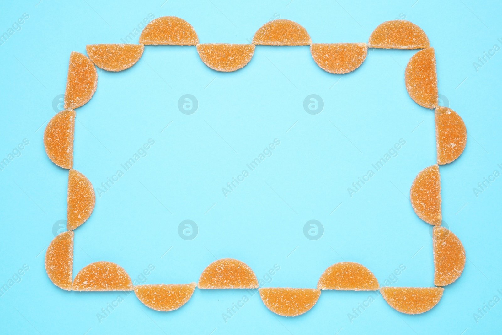 Photo of Frame made with orange marmalade candies on light blue background, flat lay. Space for text