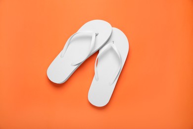 Stylish white flip flops on orange background, top view