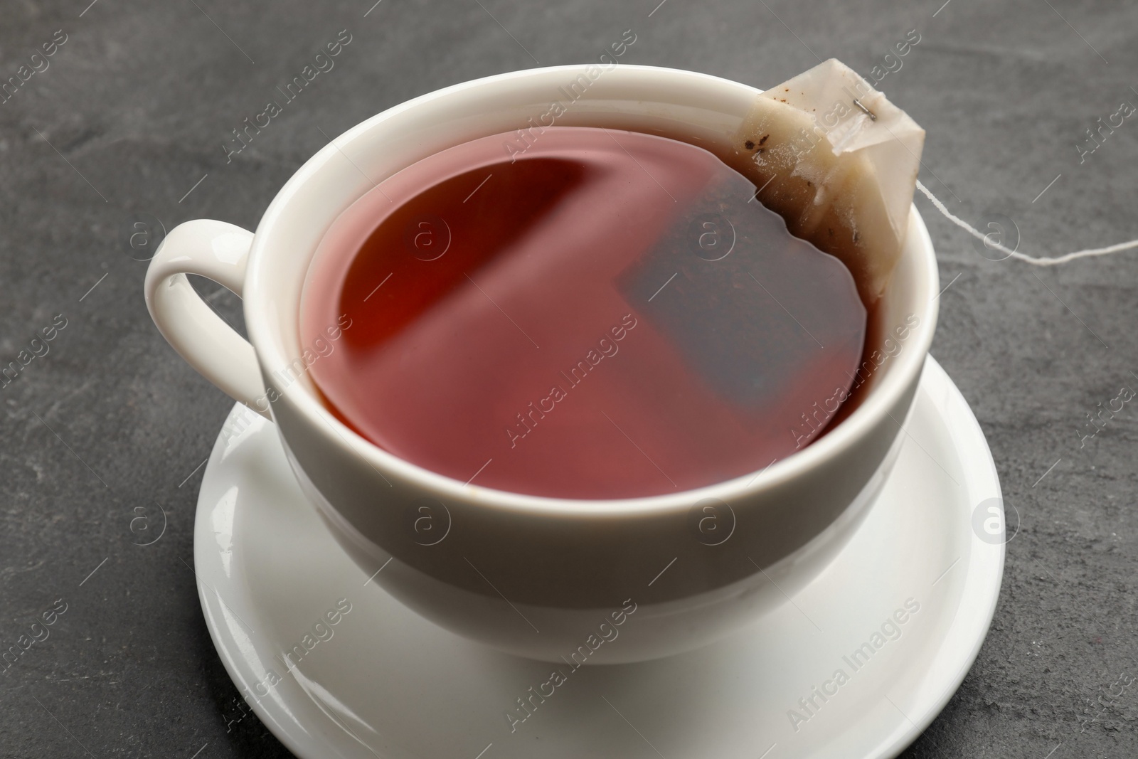 Photo of Tea bag in cup with hot drink on grey textured table, closeup