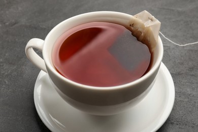 Tea bag in cup with hot drink on grey textured table, closeup