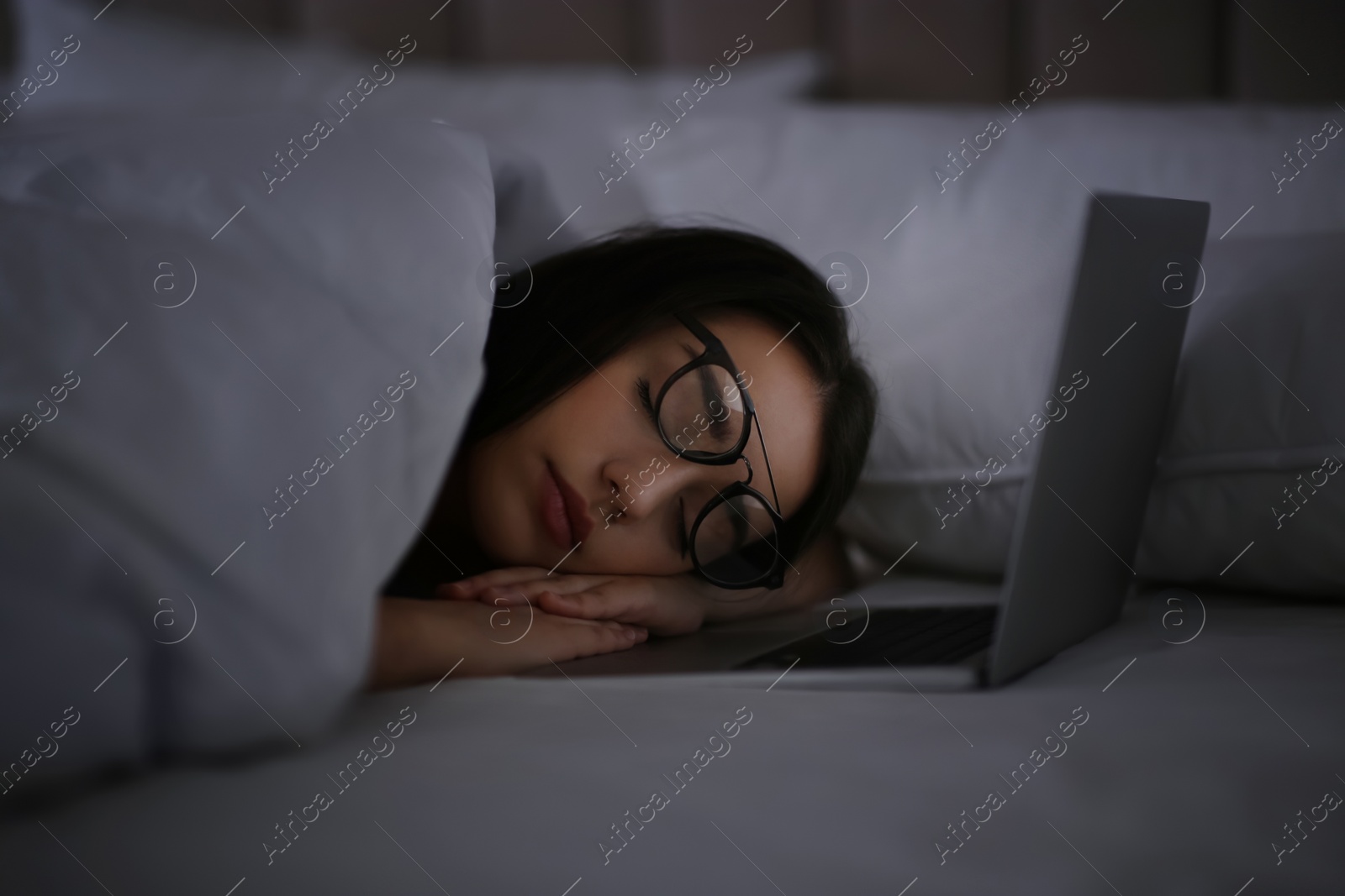 Photo of Young woman with nomophobia sleeping near laptop in bed at night