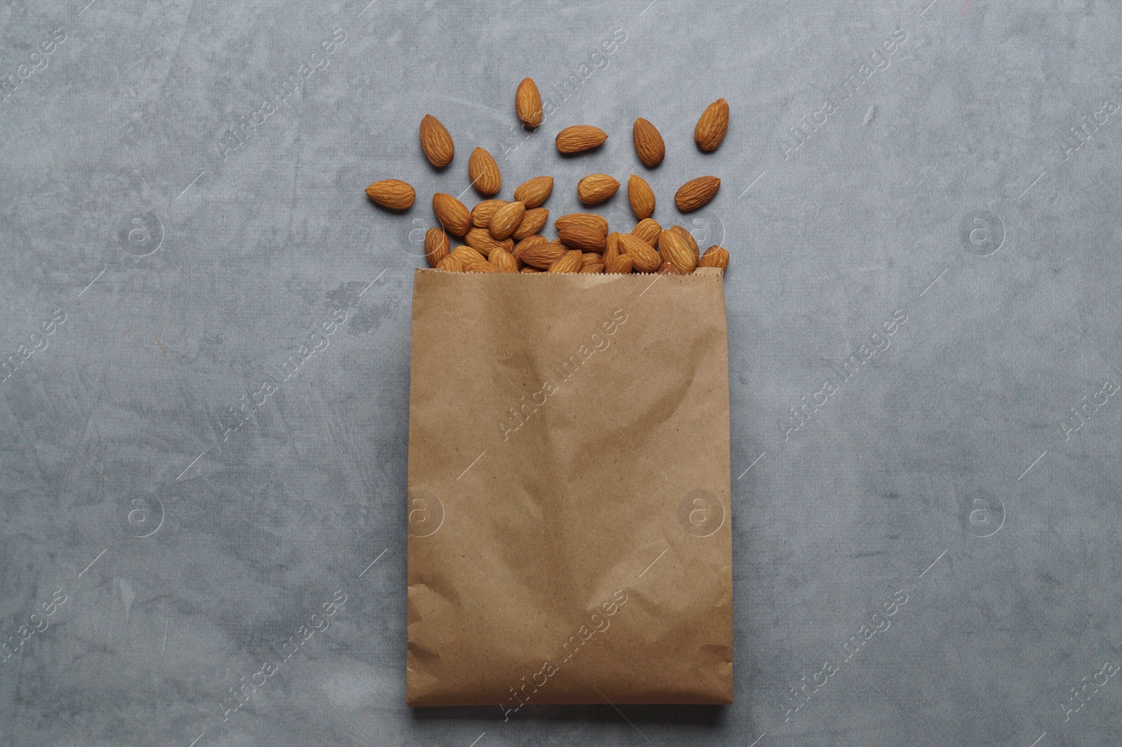 Photo of Paper bag with delicious almonds on grey table, top view