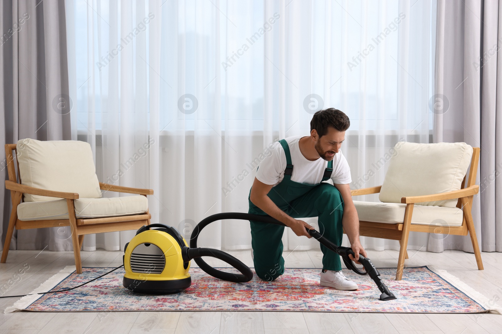 Photo of Dry cleaner's employee hoovering carpet with vacuum cleaner in room