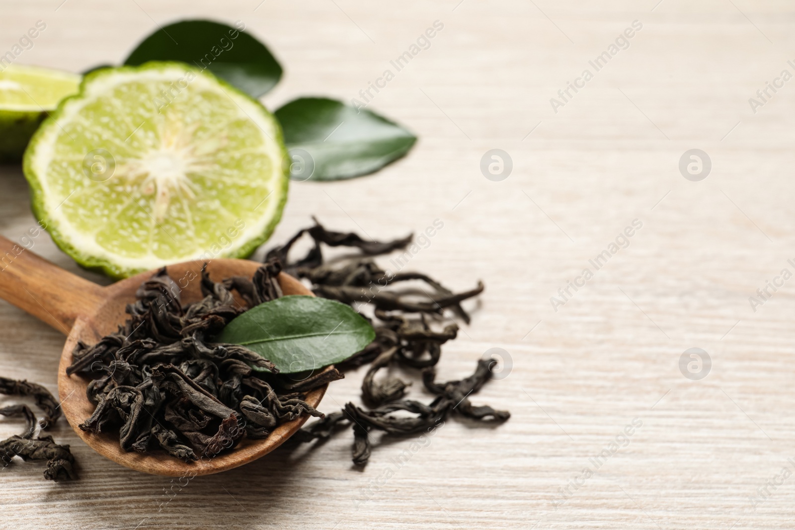 Photo of Dry bergamot tea leaves and fresh fruit on light wooden table, closeup. Space for text