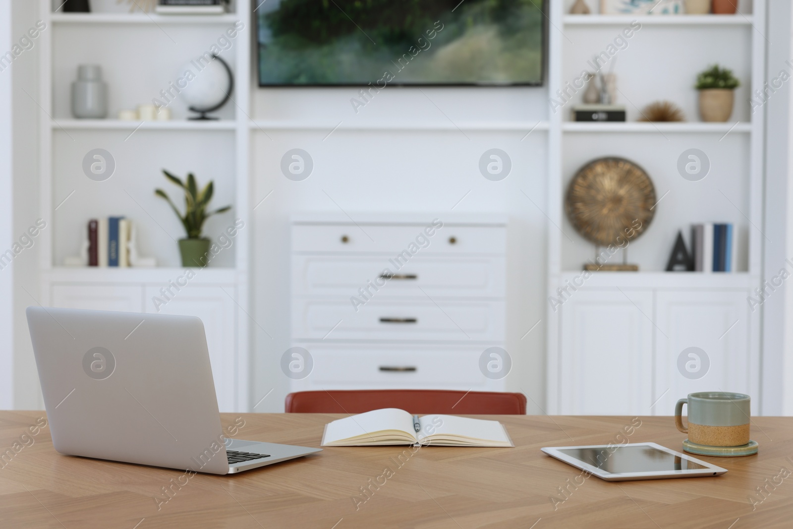 Photo of Interior design. Cosy workplace with laptop, tablet and cup on wooden table near tv area. Space for text