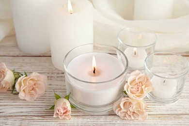 Photo of Composition with burning aromatic candles and roses on wooden table