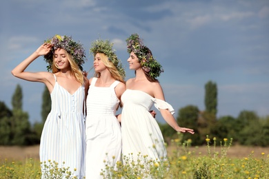 Photo of Young women wearing wreaths made of beautiful flowers in field on cloudy day