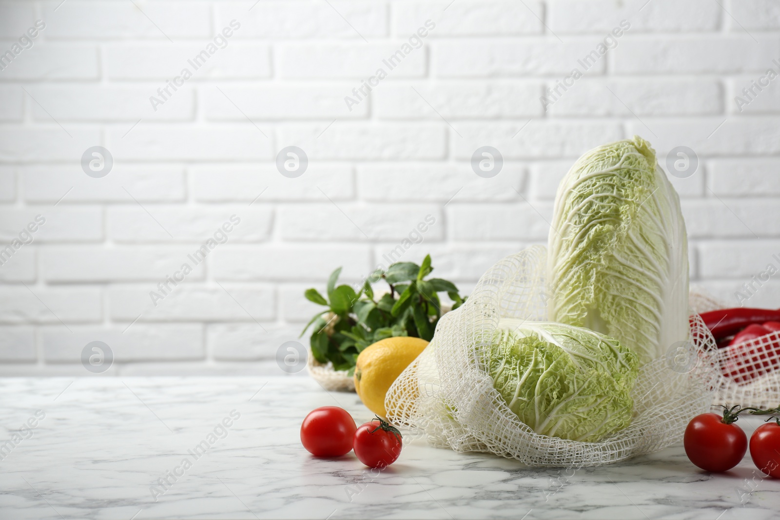 Photo of Fresh Chinese cabbages and other vegetables on white marble table near brick wall. Space for text