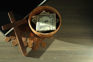 Photo of Donate and give concept. Bowl with coins, dollar banknotes, cross and Bible on wooden table, above view. Space for text