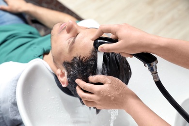 Stylist washing client's hair at sink in beauty salon