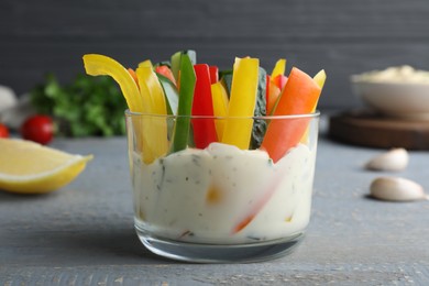 Photo of Fresh raw vegetable sticks with sauce on grey wooden table